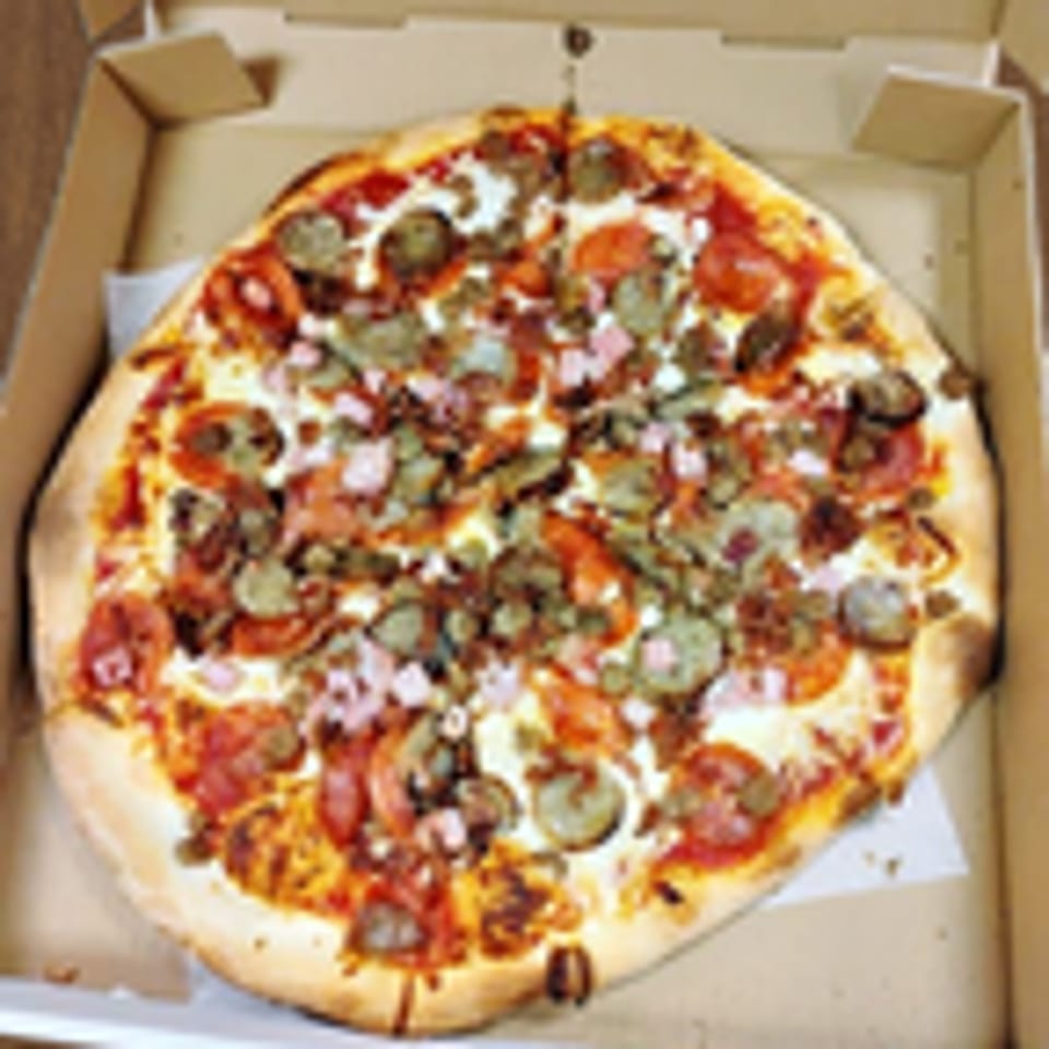 A large, round pizza with pepperoni, sausage, ham, and mushrooms in a cardboard box.